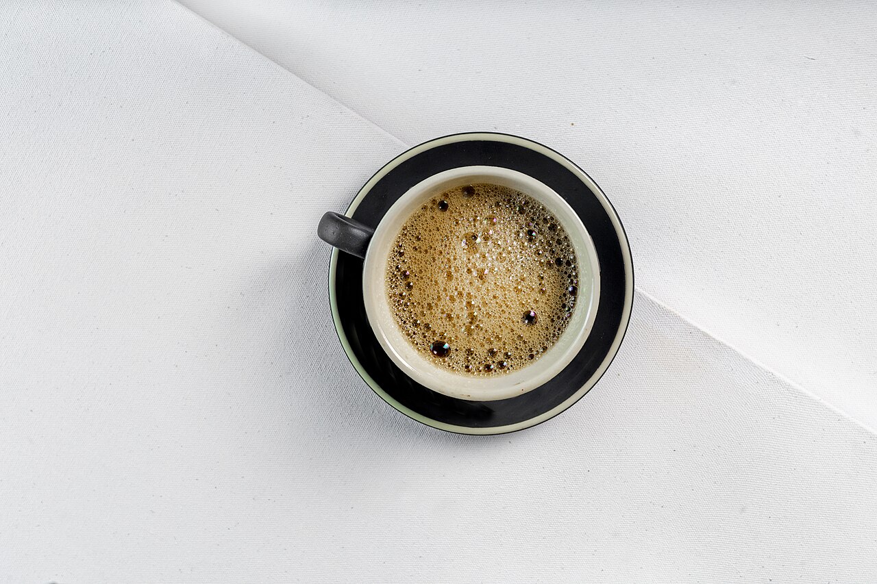 Cup of black coffee seen from above on a white tablecloth