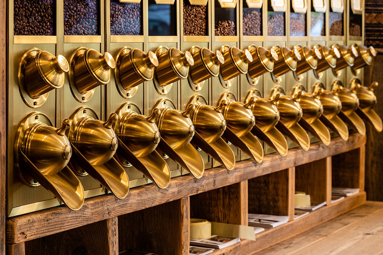 Row of brass bean dispensers above wooden shelves