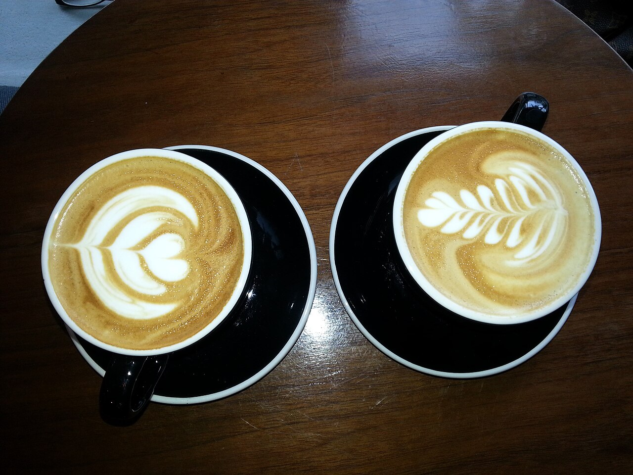 Two lattes with heart and leaf patterns on a wooden table